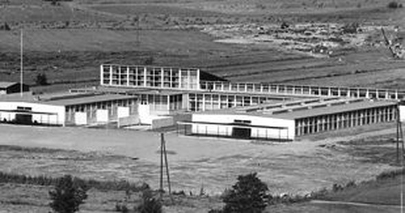 Eksteriöörikuva Tapiolan kansakoulusta. Kaukaa otetussa kuvassa matala koulurakennus peltojen ympäröimänä.
