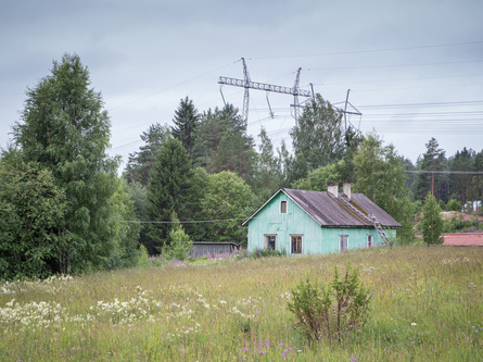 Hylätty vanha puutalo niityllä sähkölinjojen alla