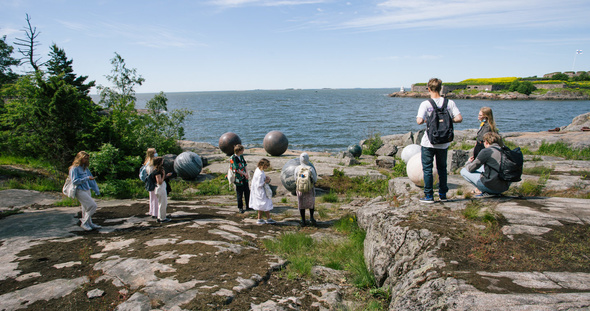 Ryhmä nuoria seisoo aurinkoisella kalliolla meren rannalla.