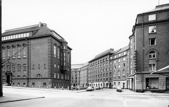 Mustavalkoinen valokuva loivasti kaartuvasta katunäkymästä, jota ympäröi tiiliset kerrostalorakennukset.
