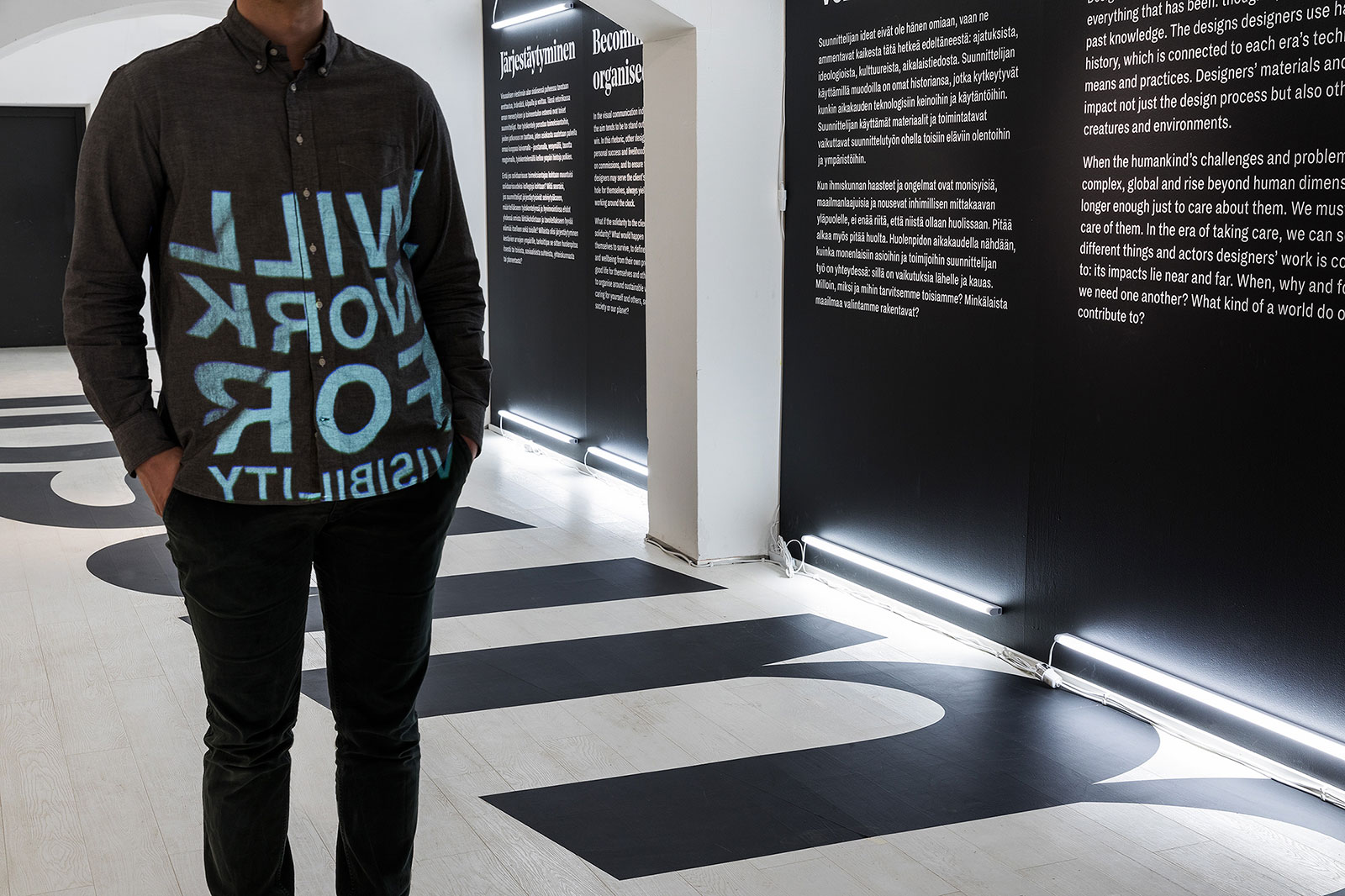 Kuva Designmuseon Grafia-näyttelystä. Etualalla ihminen, jolla graafinen teksti paidassa.